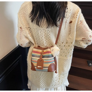 Detail of colorful woven straw bucket bag with brown leather trim and plush pompom charm