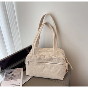 Detail of a minimalist beige nylon tote bag with drawstring sides and zipper pockets