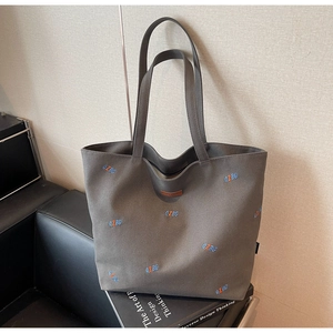 Detailed close-up of grey canvas tote bag featuring embroidered letters and leather logo