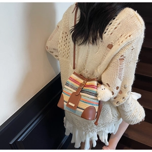 Detailed shot of multi-colored woven bucket bag with brown leather strap and plush charm