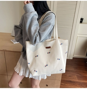 Detail of off-white canvas tote bag with QZBG lettering and leather patch on shoulder