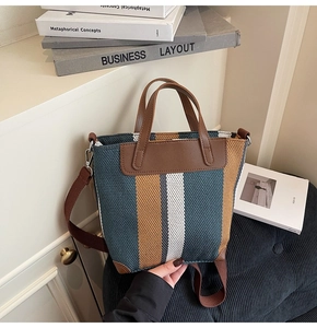 Detail of striped canvas tote featuring woven fabric, brown leather trim, and metal buckles