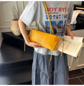 Détail du sac baguette en cuir verni jaune gingembre avec logo métallique et nœuds décoratifs