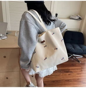 Close-up of cream canvas tote bag with embroidered letters and brown leather patch details