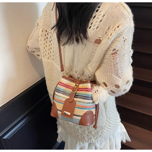 Detailed shot of striped woven bucket bag with leather trim and plush ball accessory