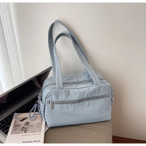 Macro detail of a light blue nylon tote bag featuring front zip pockets and texture