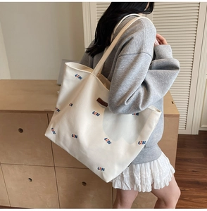 Detail of white canvas tote bag featuring red and blue letter print and leather patch