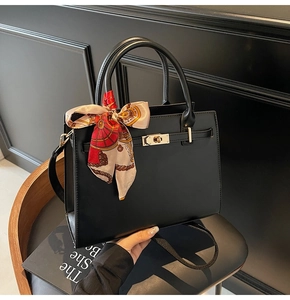 Detail of a matte black handbag with a metal turn-lock and floral silk scarf accessory