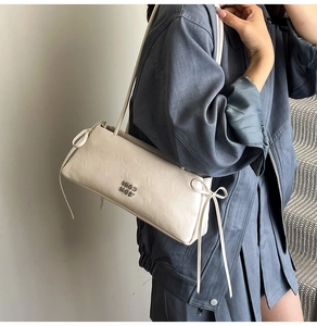 Gros plan du sac à bandoulière crème avec texture plissée, logo et nœuds déco