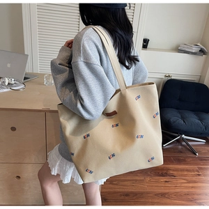 Detailed embroidery on khaki canvas tote bag worn by a model in an office setting