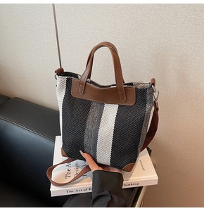 Detailed view of woven canvas tote bag with black and white stripes and brown leather trim