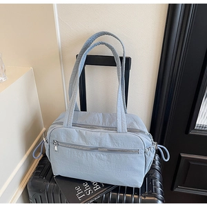 Detailed view of light blue nylon tote bag with multiple zippers on a suitcase
