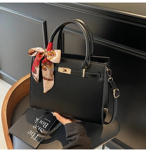 Detail of black handbag with golden swivel lock and patterned silk scarf wrapped on handle