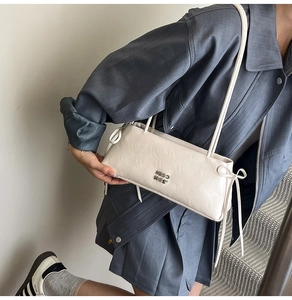 Détail du sac baguette crème avec texture cuir plissée et nœuds sur les côtés