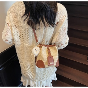 Detailed back view of a woven straw bucket bag with leather trim and white plush charm