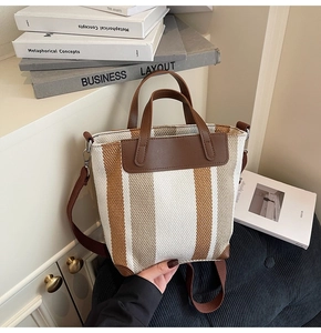 Detail of woven striped bucket bag with brown faux leather handles and adjustable strap