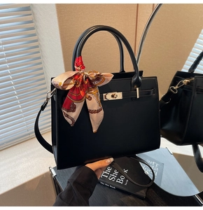 Detail of black matte leather handbag featuring a metal turn-lock and red floral scarf