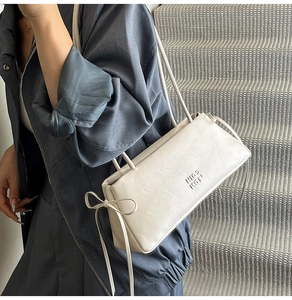 Détail d'un sac baguette beige avec texture cuir et nœud papillon sur une fine bandoulière