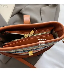 Close-up of smooth gold metal zipper and brown leather trim on striped woven bucket bag