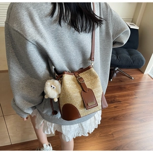 Detail of woven straw bucket bag with brown leather trim and fuzzy monster charm