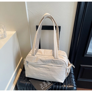 Detail of cream nylon tote bag with side drawstring pockets on a black suitcase