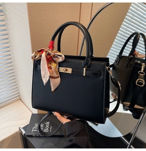 Detail of black synthetic leather handbag with scarf handle and golden twist lock closure
