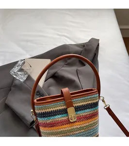 Detail of colorful woven bucket bag with brown leather handle and gold buckle closure