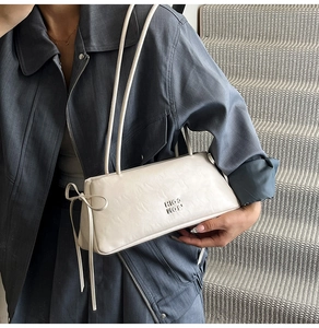 Détail d'un sac baguette en cuir plissé beige avec logo BOH et nœud sur une veste bleue
