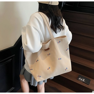 Detail view of large beige canvas tote bag with letter print and leather logo patch