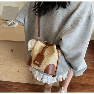 Detail of woven straw bucket bag with leather trim and cute charm on gray sweatshirt