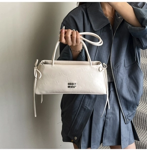 Détail du sac baguette en cuir blanc crème avec logo COIN en métal et nœuds en ruban