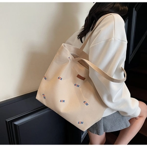 Detail of canvas tote bag showing QZBG embroidery and leather logo patch on beige fabric