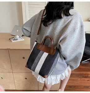 Detail of striped canvas tote bag with brown leather handles on a wooden desk