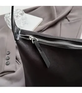 Detailed close-up of smooth silver metal zipper and black leather pull on canvas shoulder bag