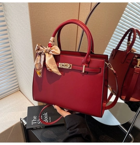 Close-up of deep red handbag with golden twist lock and elegant floral silk scarf