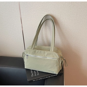 Detail view of a light green nylon tote bag with drawstring side knots on a sofa