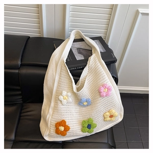 Close-up of white knitted tote bag with colorful 3D crochet flowers on a leather surface