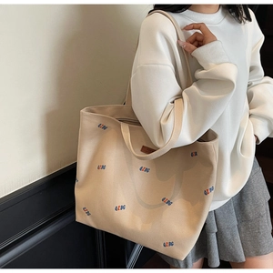 Detailed side view of a large beige canvas tote bag with colorful QZBG letter embroidery