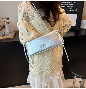 Détail du sac à bandoulière argenté rectangulaire avec logo et bandoulière à nœuds