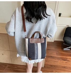 Rear view of a striped canvas bucket bag with brown leather trim and a long shoulder strap
