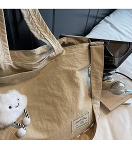 Gros plan sur le sac fourre-tout beige en nylon avec pendentif nuage sur un lit