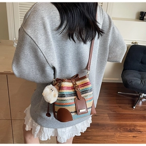 Detail of colorful rainbow woven straw bucket bag with brown leather trim and plush charm