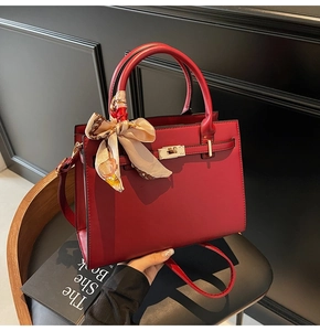 Detail of a dark red faux leather handbag with golden lock and patterned silk scarf