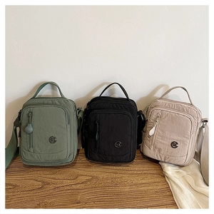 Detail of waterproof nylon crossbody bag with functional front zippers and round metal logo