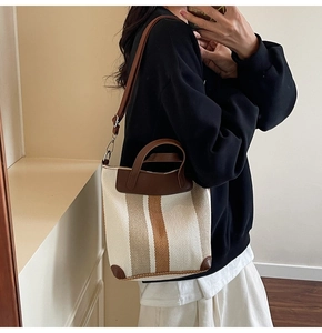 Close-up of canvas bucket bag featuring vertical stripes and brown leather trim details