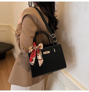 Detail of a black leather handbag with gold clasp, top handle, and decorative silk scarf