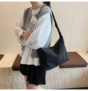 Detail of minimalist black nylon shoulder bag with leather strap and metal logo plaque
