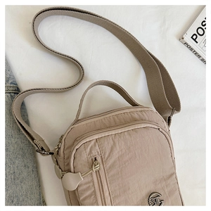 Close-up of beige nylon crossbody bag with multiple zippers and wide woven shoulder strap