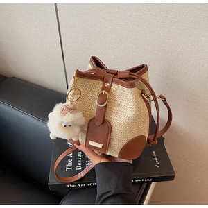 Detail of hand-woven straw bucket bag with dark brown leather trim and sheep pendant