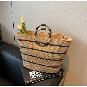 Close-up of woven straw tote bag with black stripes and circular handles in a studio setting